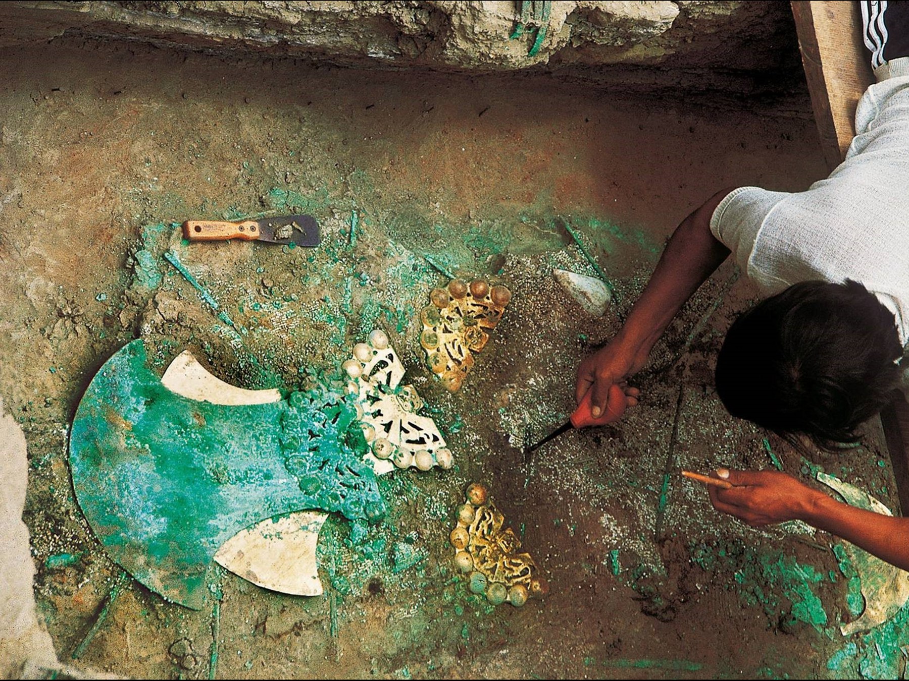 Coxal em cobre dourado (Tumbago) com duas iguanas e sete esferas como encontrado na escavação.